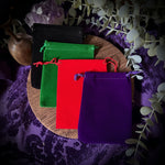 Colorful velvet bags on a wooden board with purple fabric and eucalyptus leaves in the background