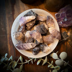 Amethyst crystals in a bowl on a wooden surface with a pentagram symbol and eucalyptus leaves.