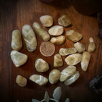 Collection of green chevron stones on a wooden surface with a penny for scale, next to a pink candle and a crystal.