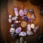 Amethyst crystals on a wooden surface with a pink candle and brass container.