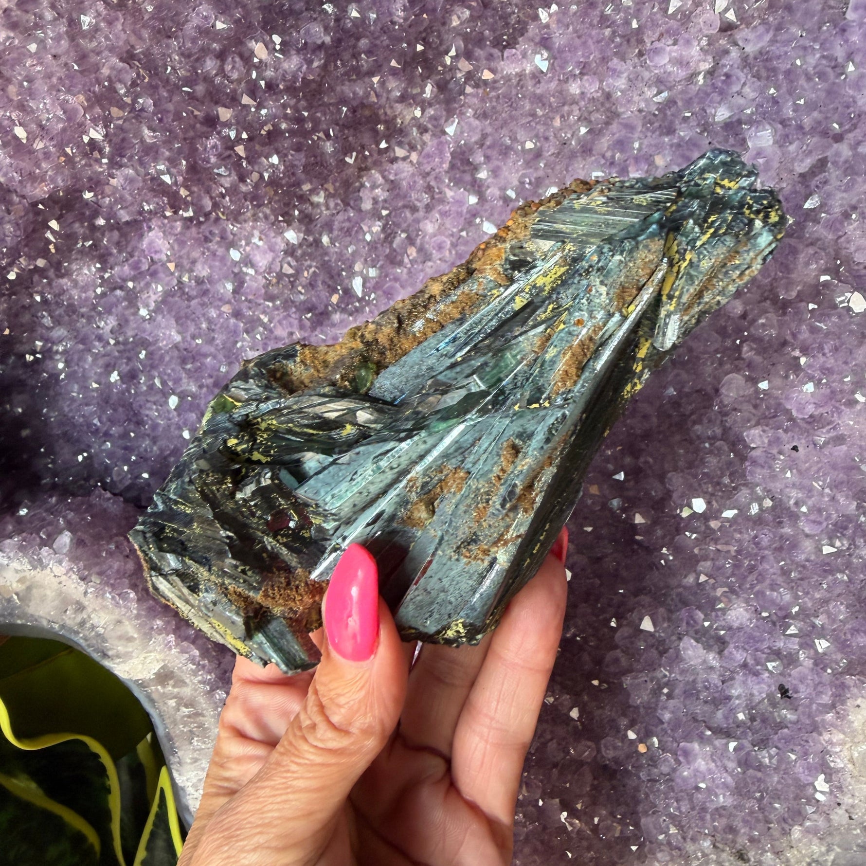 Green vivianite crystal being held by a hand.