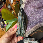 Green vivianite crystal being held by a hand.