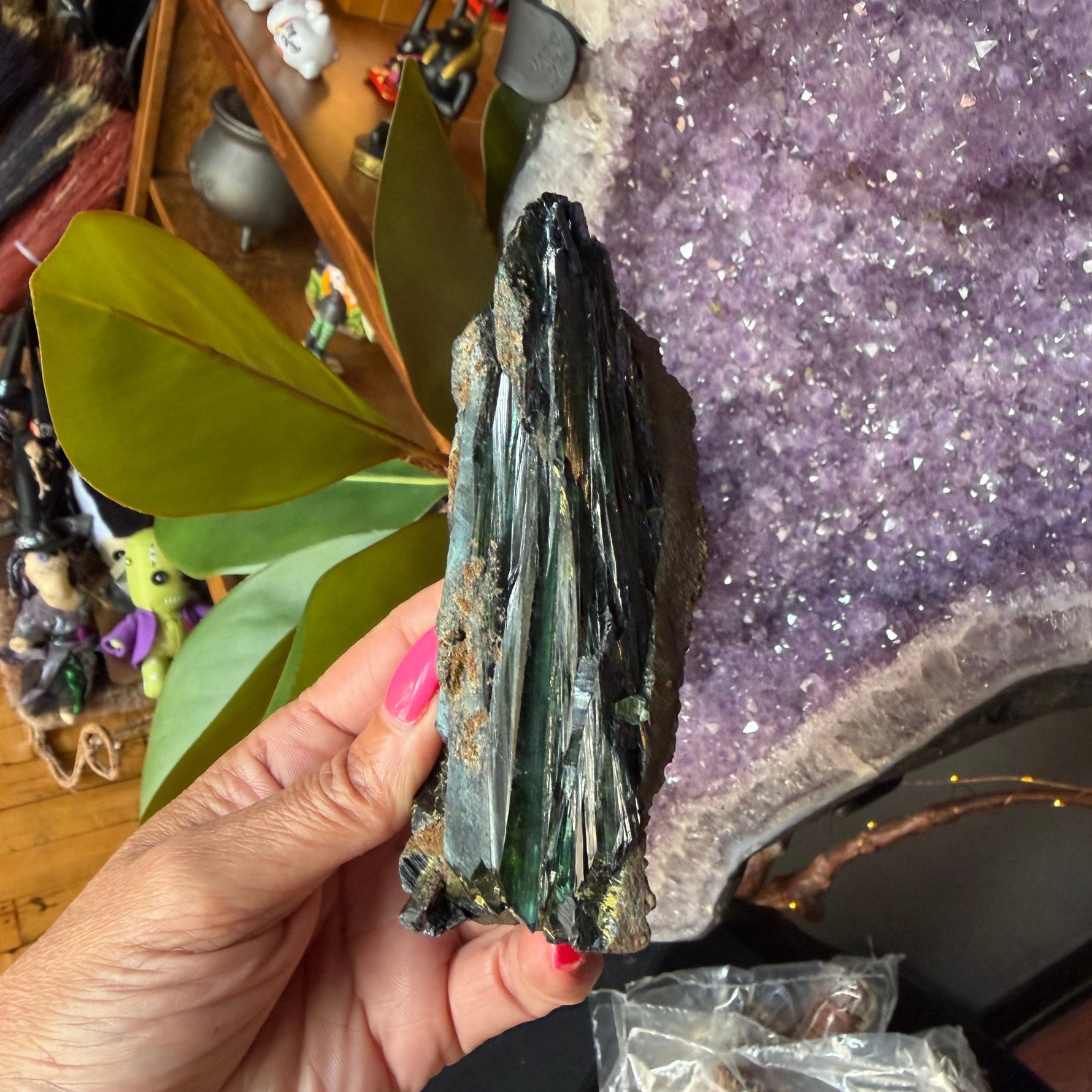 Green vivianite crystal being held by a hand.