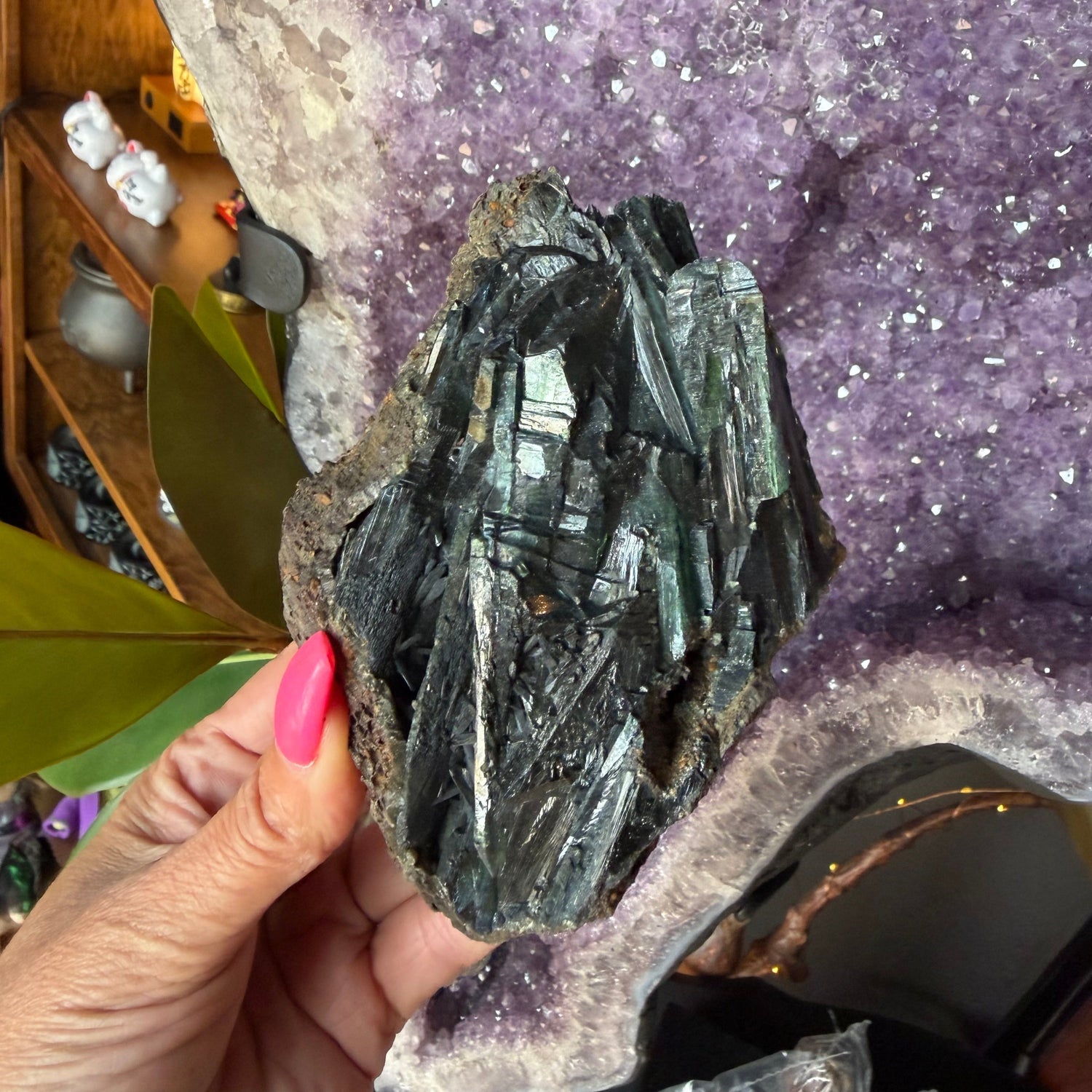 Person holding a dark crystal rock in front of a large amethyst crystal