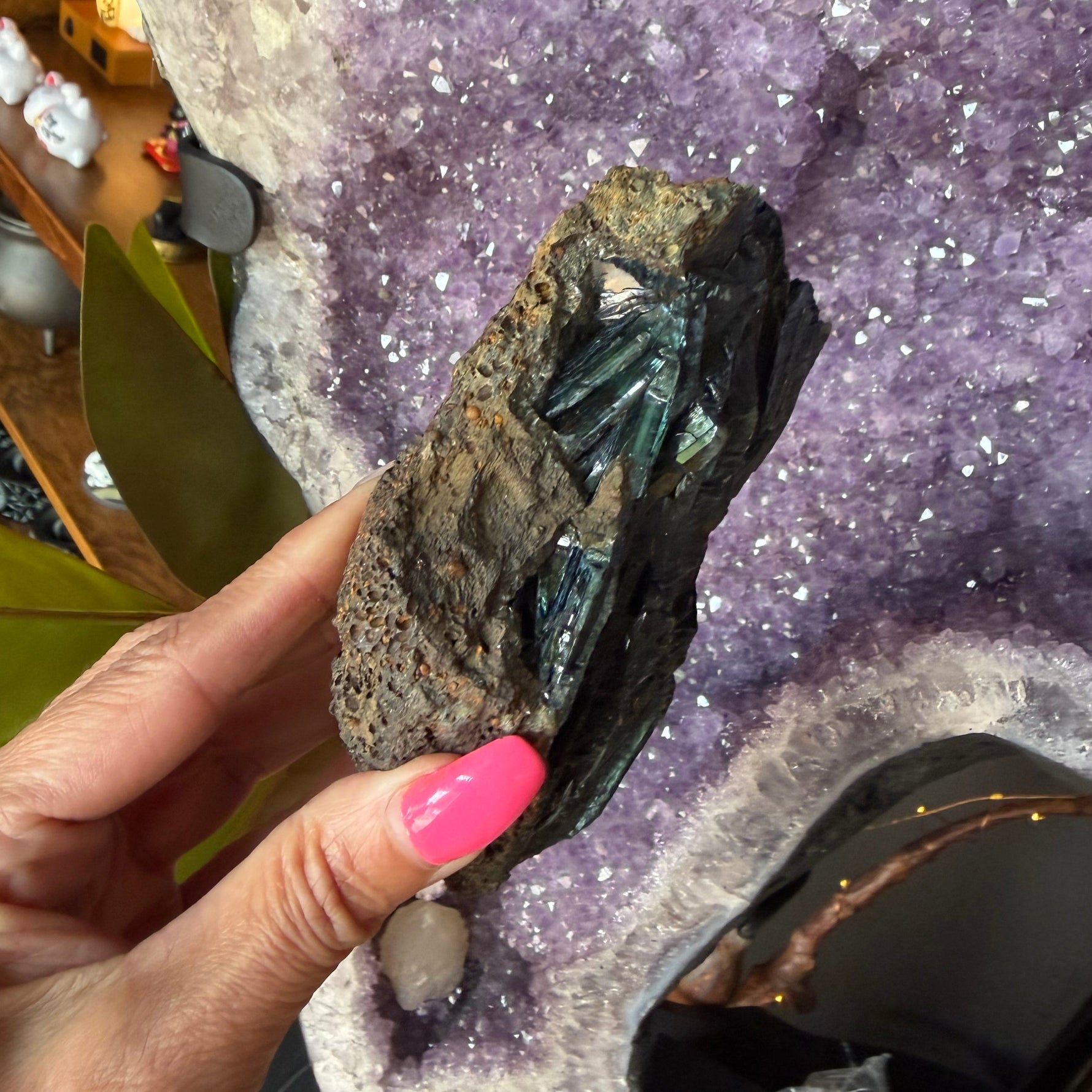 Hand holding a stone with a large amethyst crystal in the background
