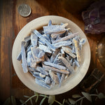 Decorative display with crystals in a bowl, candles, and plants on a wooden surface