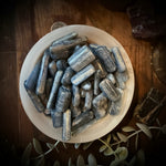 Small bowl filled with blue kyanite crystals  on a wooden surface with crystals and leaves.