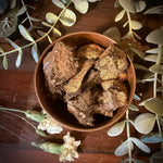 Gold lodestone in a brown bowl surrounded by greenery on a wooden surface