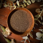 Wooden bowl filled with gold magnetic sand on a decorative surface with leaves and flowers.