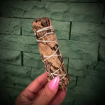 Stick of wrapped black sage being held by a hand on a green background.