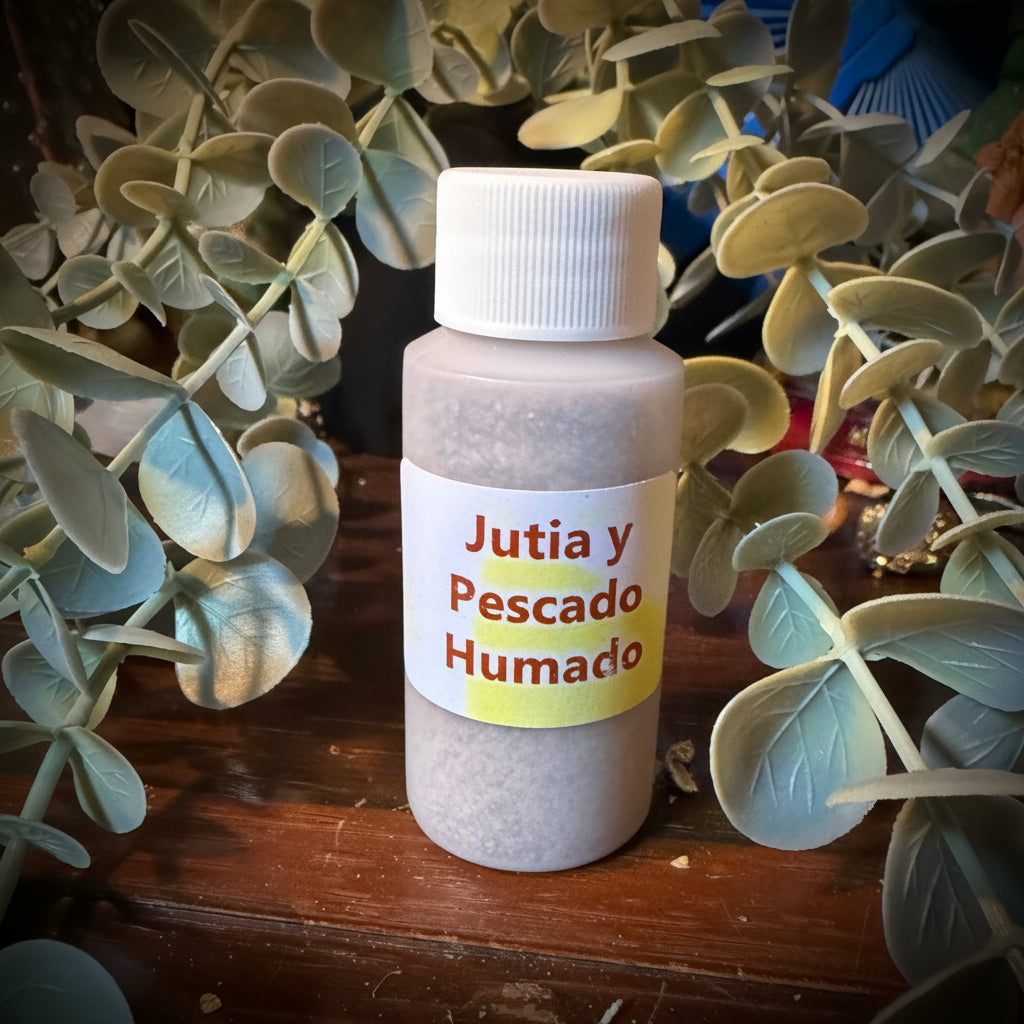 A small plastic bottle labeled 'Jutia y Pescado Humado' in red text on a white label with a yellow band, placed on a dark wooden surface surrounded by green eucalyptus leaves.