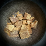 Chopped brown honey amber resin chunks placed inside a dark gray stone mortar bowl.