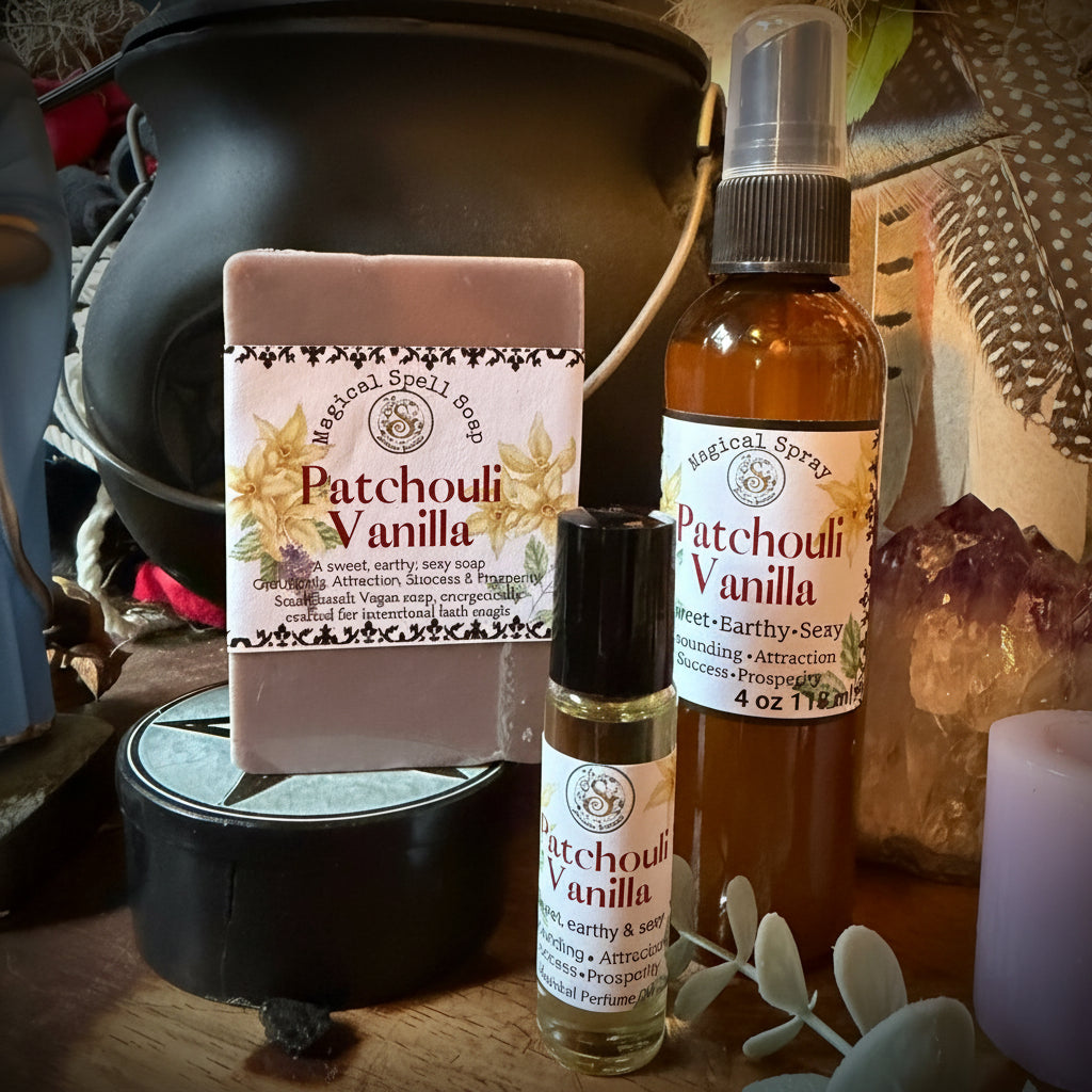 A bath and body gift set from Sweet Wildflower Soap featuring a Patchouli Vanilla soap bar, a matching spray bottle, and a roller bottle, arranged on a rustic wooden surface with a black cauldron and dried botanicals.