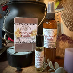 A bath and body gift set from Sweet Wildflower Soap featuring a Patchouli Vanilla soap bar, a matching spray bottle, and a roller bottle, arranged on a rustic wooden surface with a black cauldron and dried botanicals.