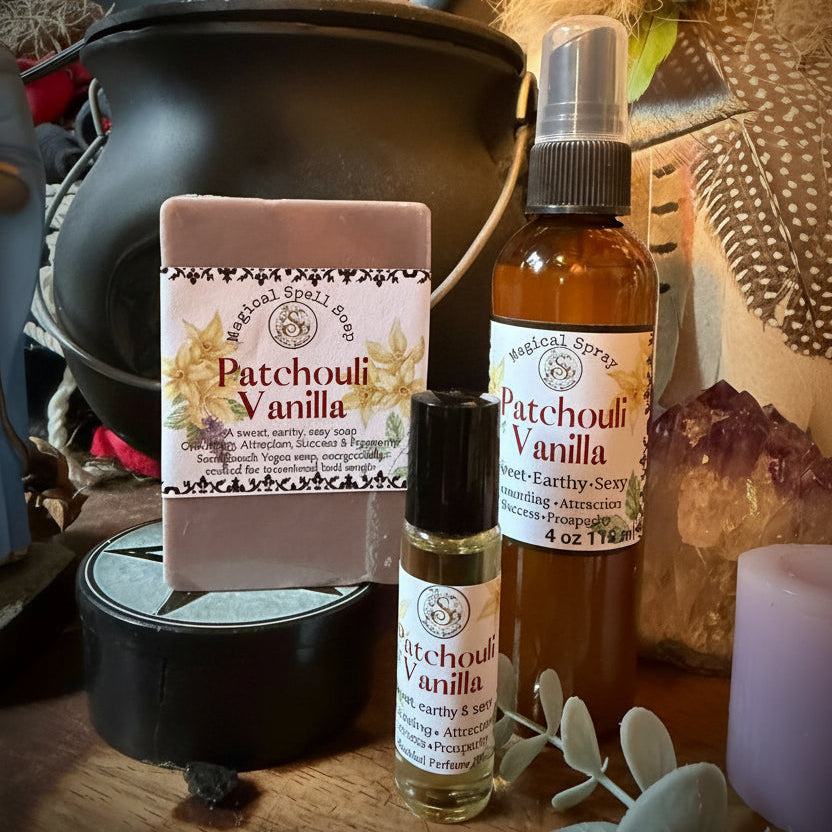 A bath and body gift set from Sweet Wildflower Soap featuring a Patchouli Vanilla soap bar, a matching spray bottle, and a roller bottle, arranged on a rustic wooden surface with a black cauldron and dried botanicals.