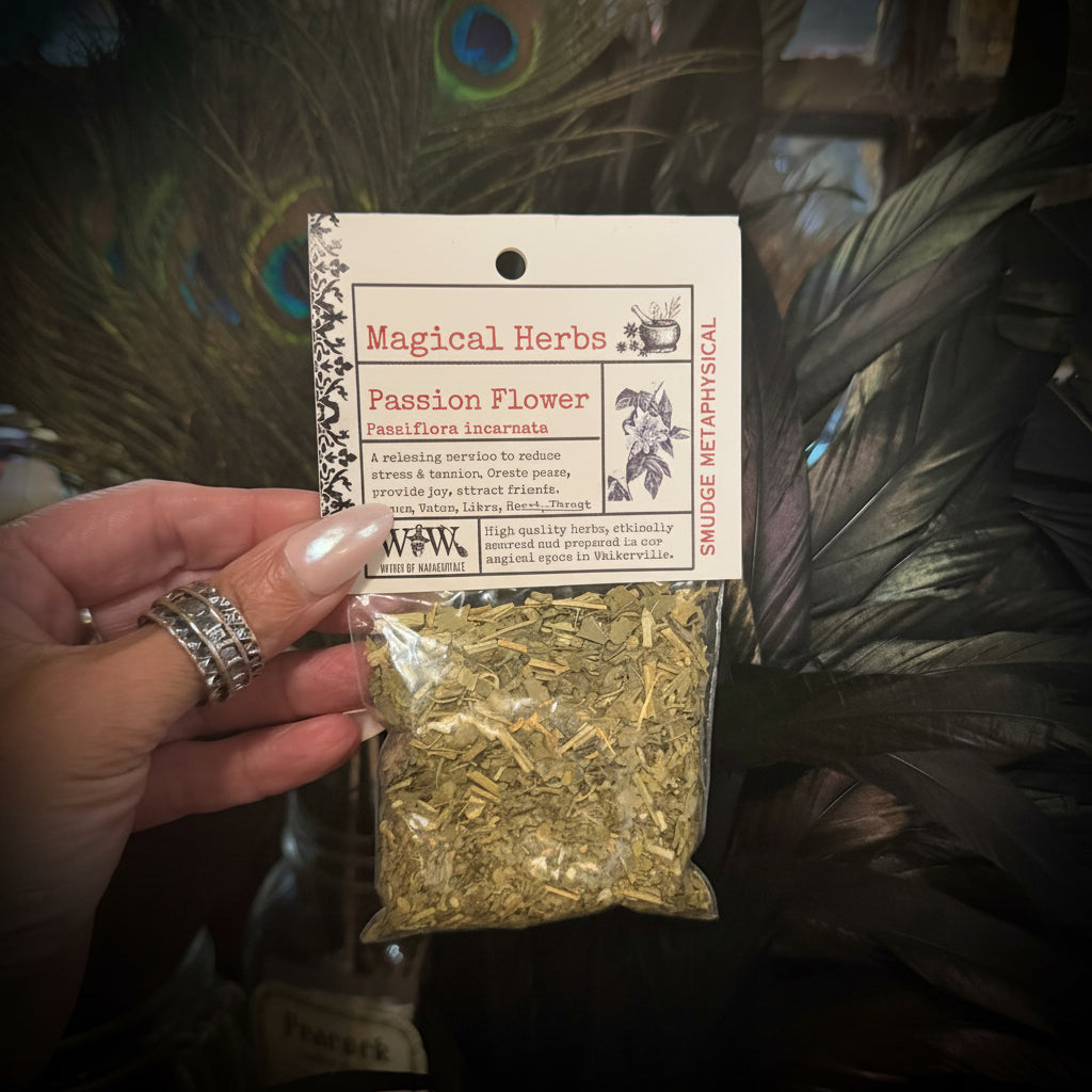 A hand holding a small clear plastic bag of dried 'Passion Flower' herbs with a white paper header card labeled 'Magical Herbs'. The background is a decorative display with peacock feathers and glass jars.