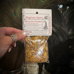 A hand holds a small clear plastic bag of dried 'Mullein Flower' herbs with a white paper header card. The background is filled with decorative dark feathers and glass jars.