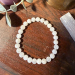 A beaded stretch bracelet made of round, polished white stone beads with natural inclusions, displayed on a dark wooden surface with decorative props.