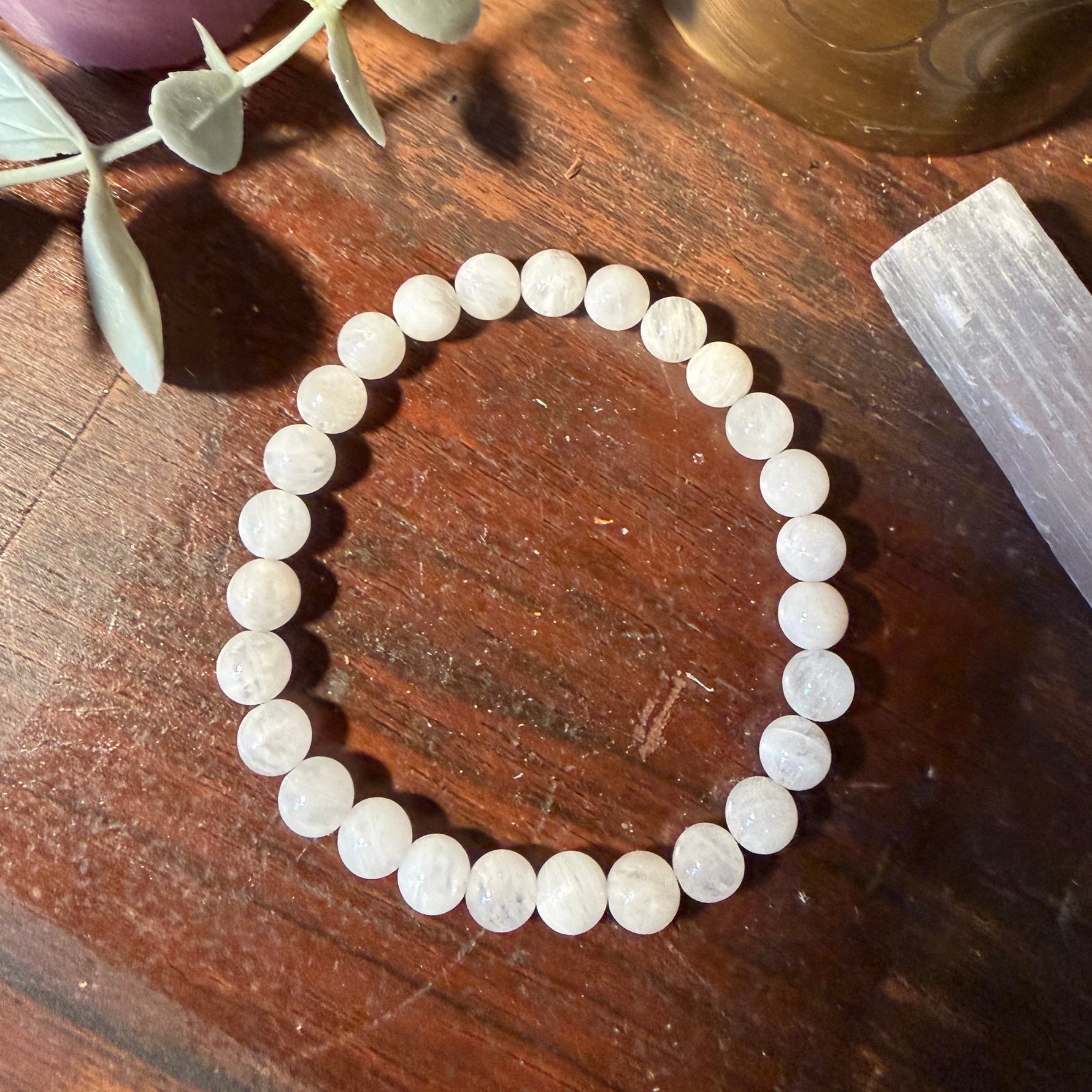 A beaded stretch bracelet made of round, polished white stone beads with natural inclusions, displayed on a dark wooden surface with decorative props.