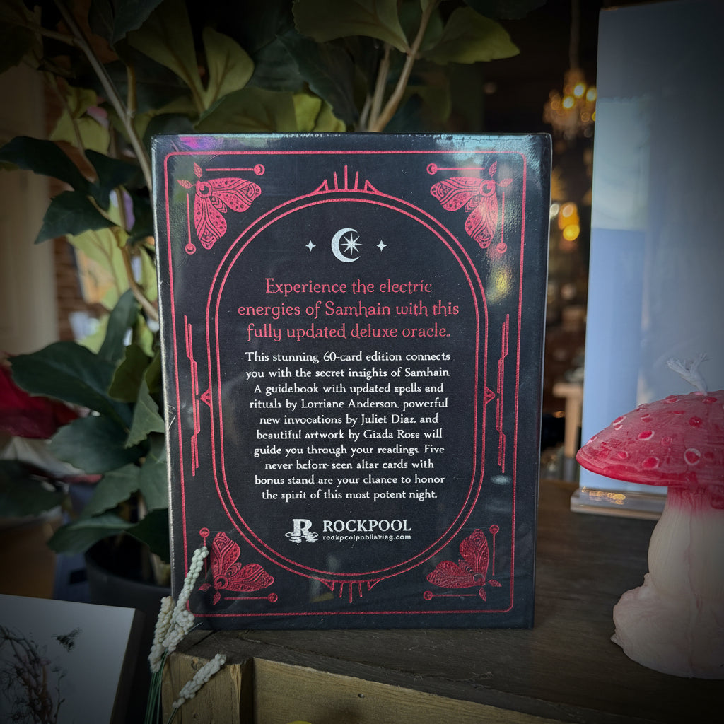 A boxed book or card set titled 'The Electric Energies of Samhain' by Rockpool, displayed on a wooden shelf among plants, a pink mushroom decoration, and other decorative items.