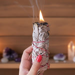 Hand holding a smoldering sage bundle with a blurred background