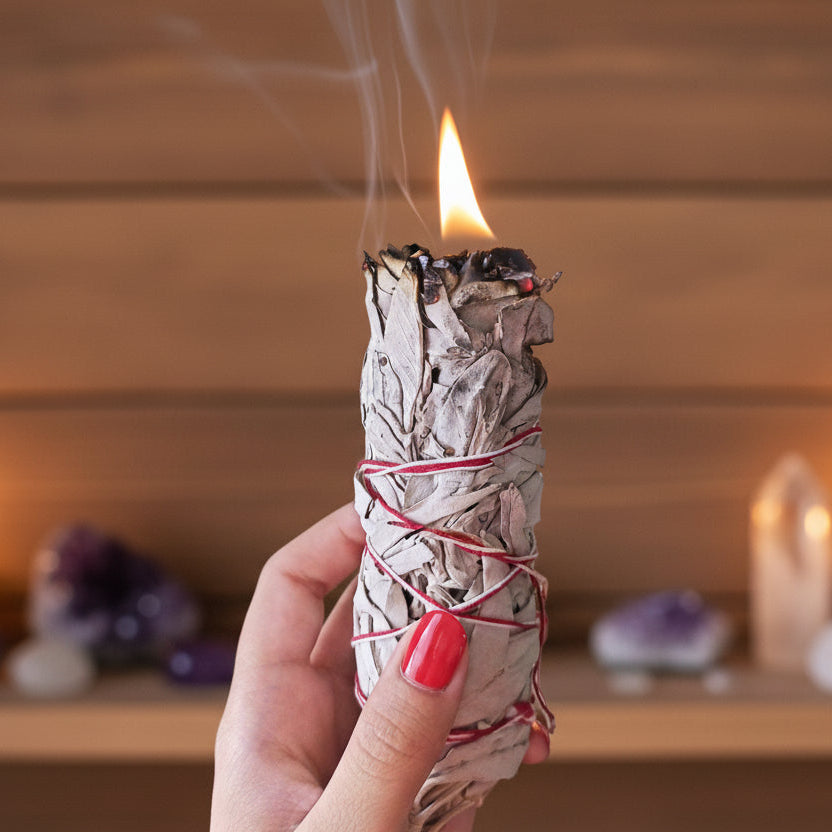 Hand holding a smoldering sage bundle with a blurred background