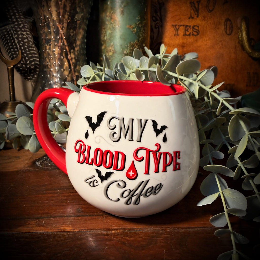 A coffee mug on a wooden table that has the saying "My blood type is coffee".