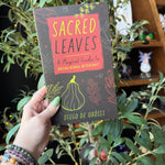 Sacred Leaves Book Being Held Up With a Tree Behind It.
