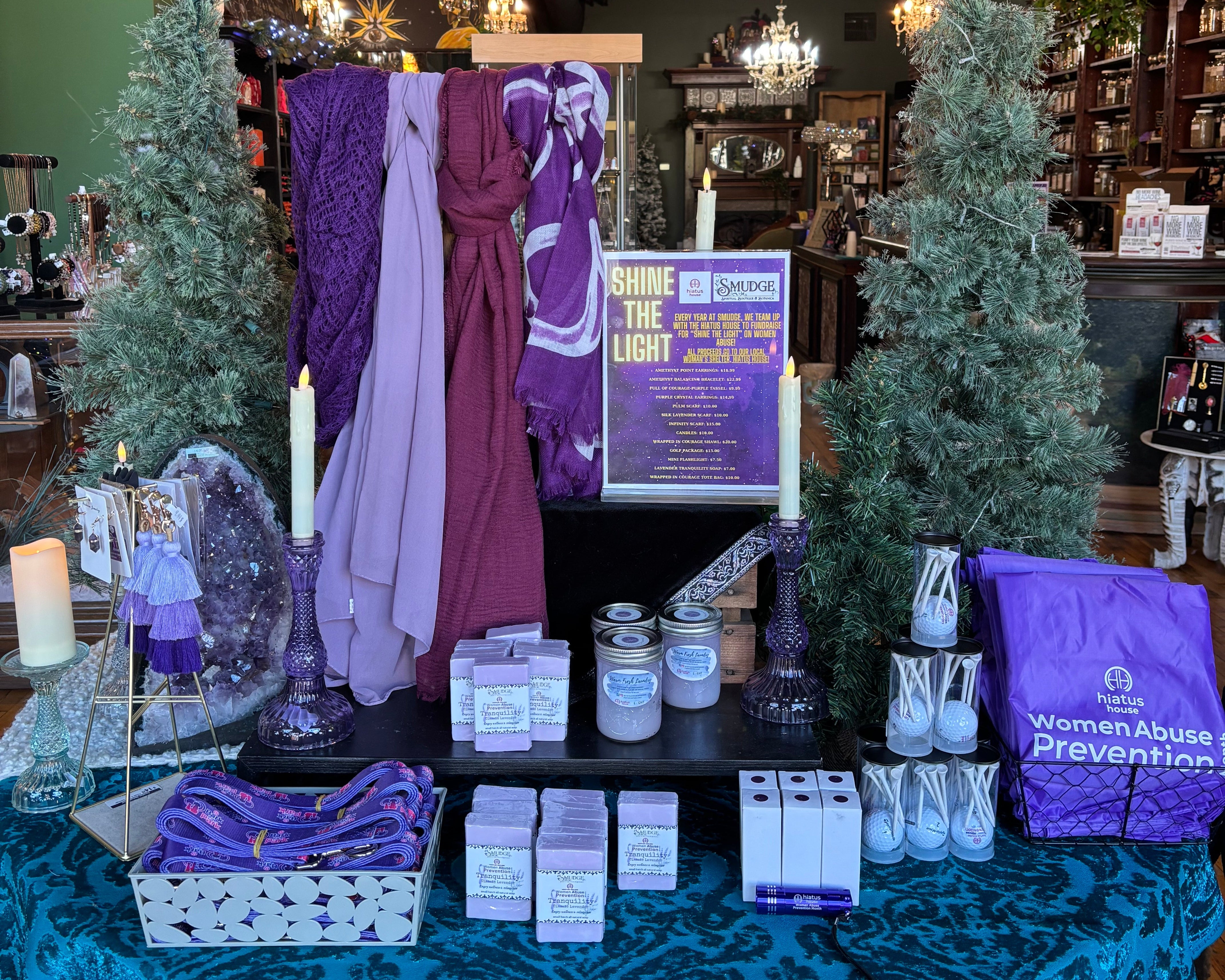Decorative setup with purple and white items on a table, surrounded by Christmas trees and a chandelier.