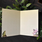 Open card with a frog and fairy design on a dark background with green leaves.