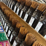 Rows of incense sticks in clear glass jars with white labels, arranged on wooden shelves in a store setting.