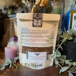 A bag of 'kyuric Immune Health & Wellness Tea' by Sagewood Spiritual Boutique is displayed on a wooden surface, surrounded by decorative props including a lit pink candle, eucalyptus leaves, and glass jars, with a 'Smudge Spiritual Boutique' watermark at the bottom.