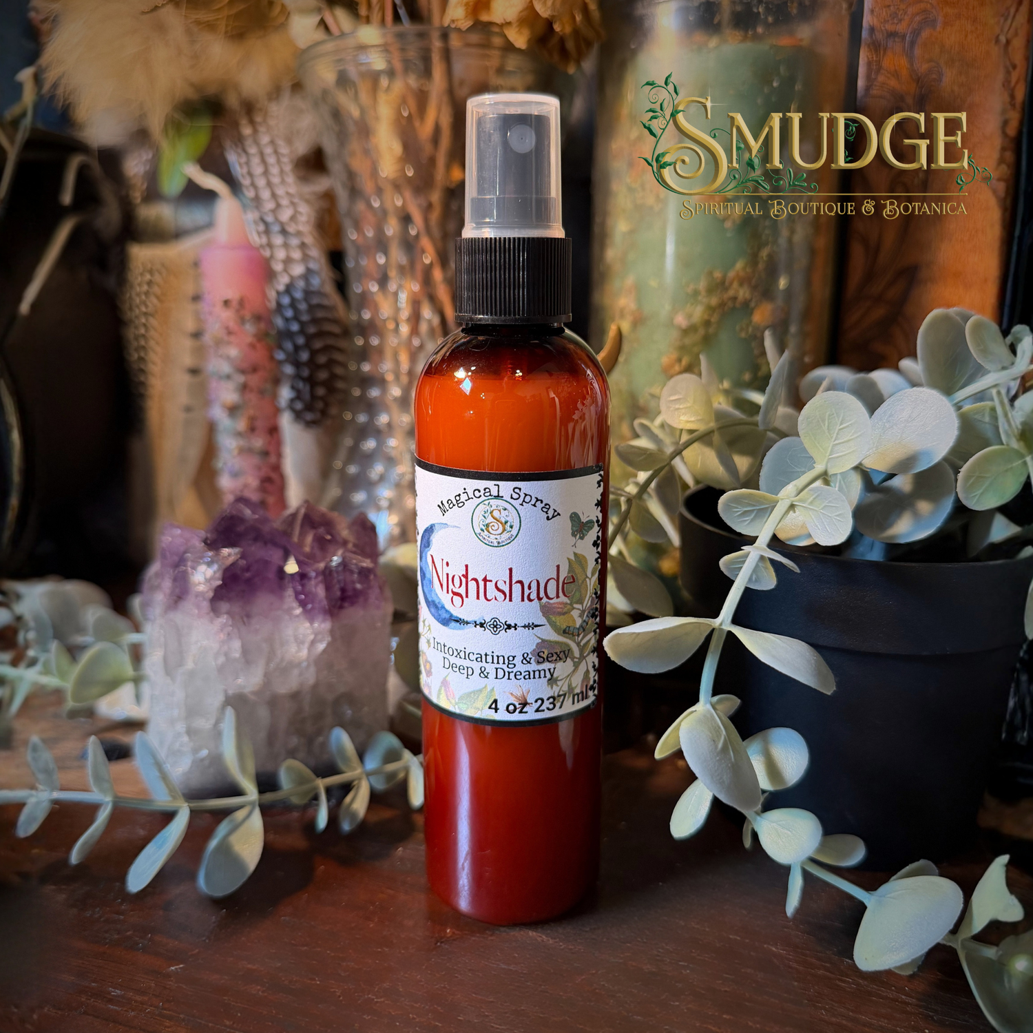 A bottle of Smudge Spiritual Boutique & Botanica Nightshade Repelling & Cleansing spray, filled with amber liquid, standing on a wooden surface surrounded by dried botanicals, a purple crystal cluster, and green eucalyptus leaves.