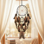 Decorative dreamcatcher with feathers hanging on a light gray wall above a modern chair.