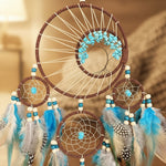 Dreamcatcher with turquoise stones, feathers, and beads on a gray background