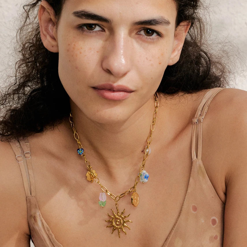 Woman wearing a gold necklace with colorful pendants against a neutral background