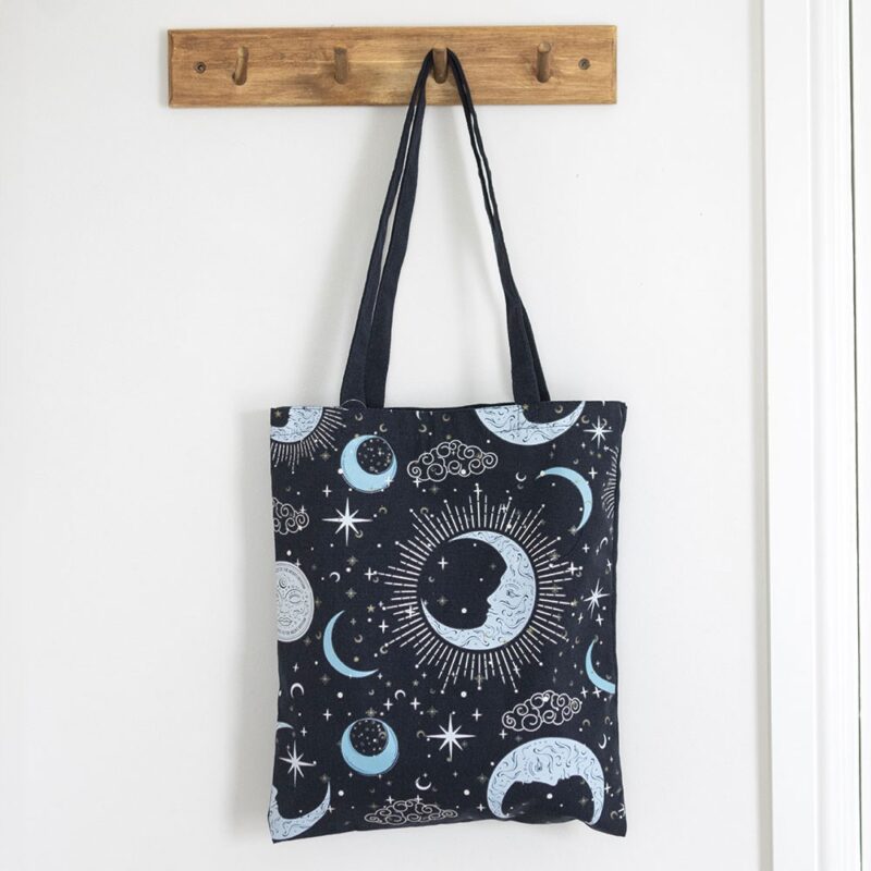 Tote bag with celestial design hanging on a wooden hook against a white wall.