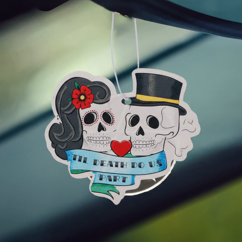 Decorative air freshener with skull design hanging from a car's rearview mirror.