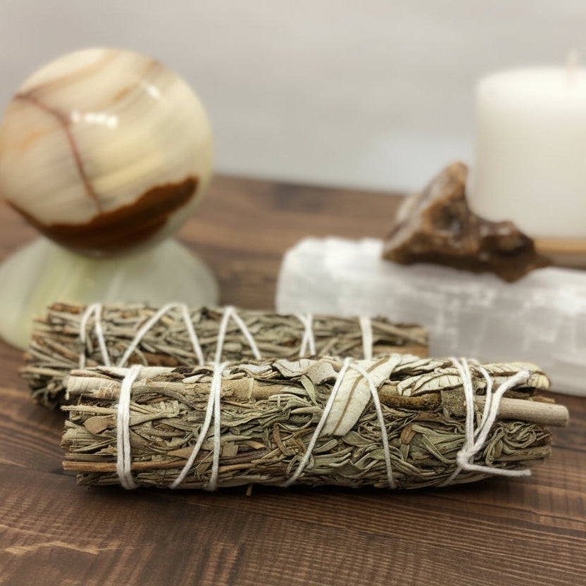 Bundled sage sticks on a wooden surface with a glass container in the background.