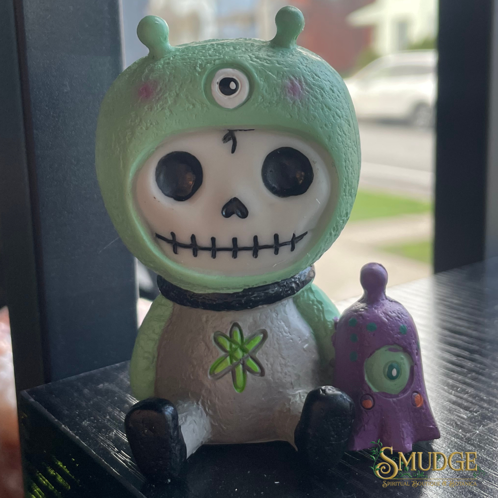 Green alien skeleton figurine with a purple tentacle toy on a reflective surface
