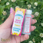 Hand holding a small bottle and packaging of 'Afrudita Mystic Musk Oil' with a green leafy background.