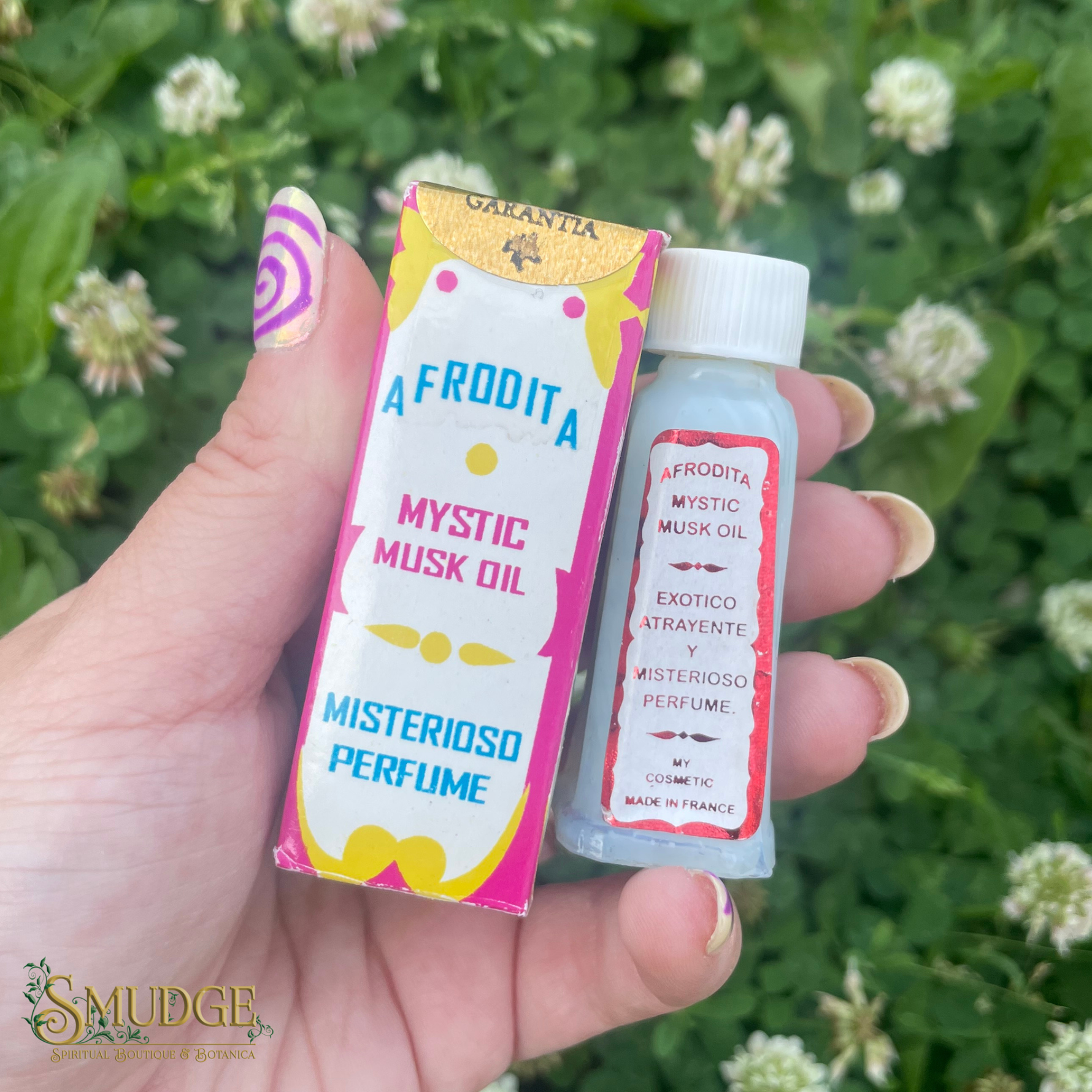 Hand holding a small bottle and packaging of 'Afrudita Mystic Musk Oil' with a green leafy background.