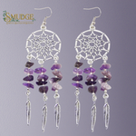 A pair of silver dreamcatcher dangle earrings with purple amethyst chips and silver feather charms, shown against a solid gray background with the Smudge brand logo in the top left corner.