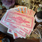 A fan of vintage-style Chinese railway ticket art prints or cards displayed on a wooden surface, surrounded by botanical props including eucalyptus leaves, a purple crystal cluster, dried roots, and a small jar. The cards feature pink/red illustrated linework and text on off-white paper.