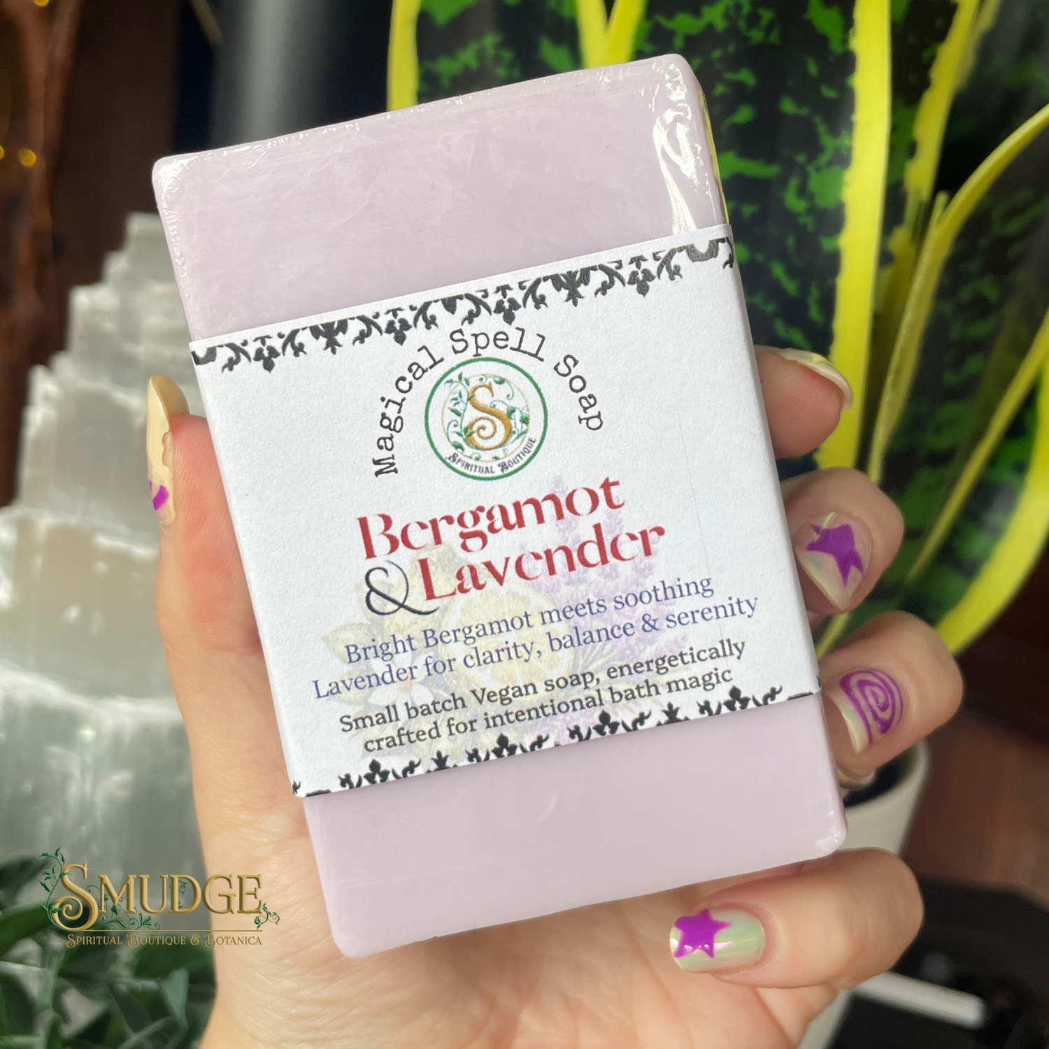 Bar of soap with 'Magical Spell Soap' label held by a hand, surrounded by greenery.