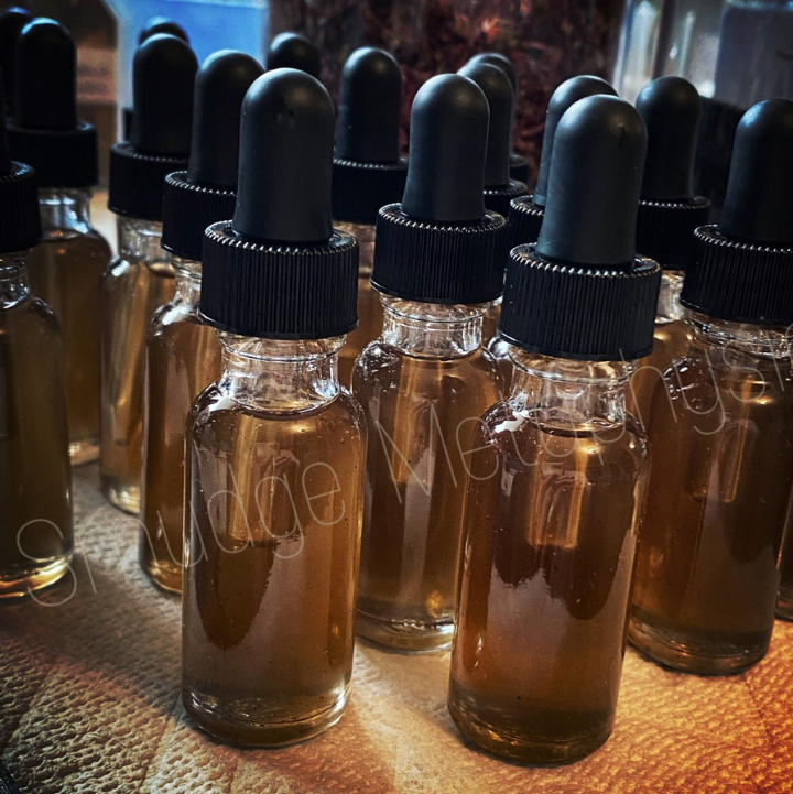 Multiple small clear glass dropper bottles filled with amber-brown liquid, arranged closely together on a textured surface. The bottles have black rubber droppers and black ribbed caps.