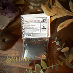 Packaged black salt with a label on a wooden surface with herbs and crystals.