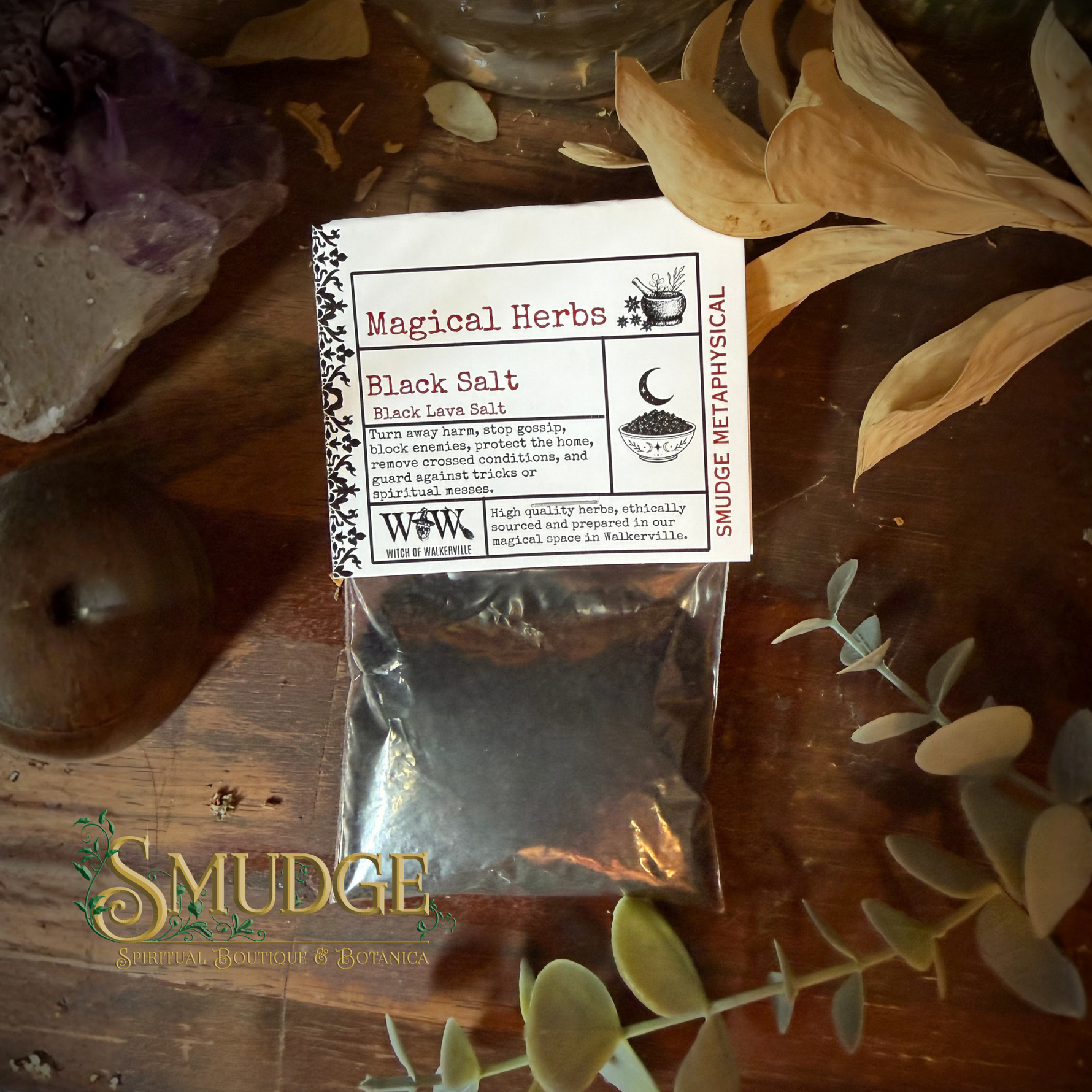 Packaged black salt with a label on a wooden surface with herbs and crystals.