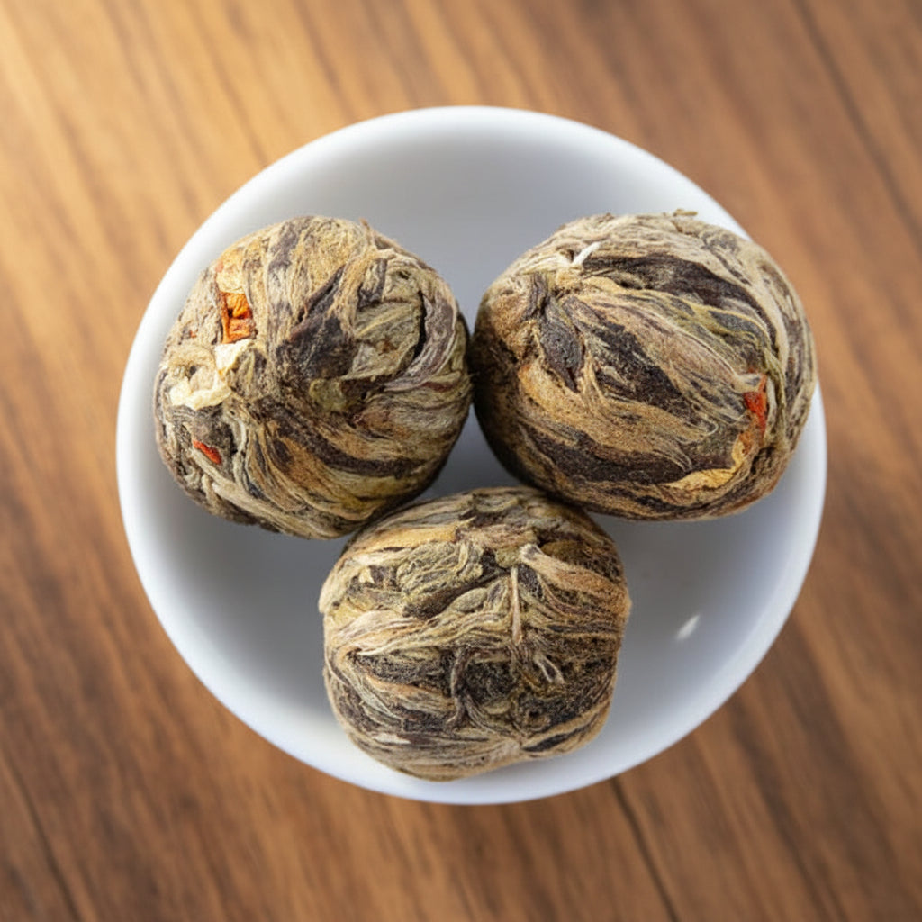 Three intricately wrapped tea balls in a white bowl with more tea balls around.