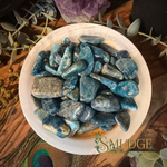Blue apatite tumbled stone in a white bowl.